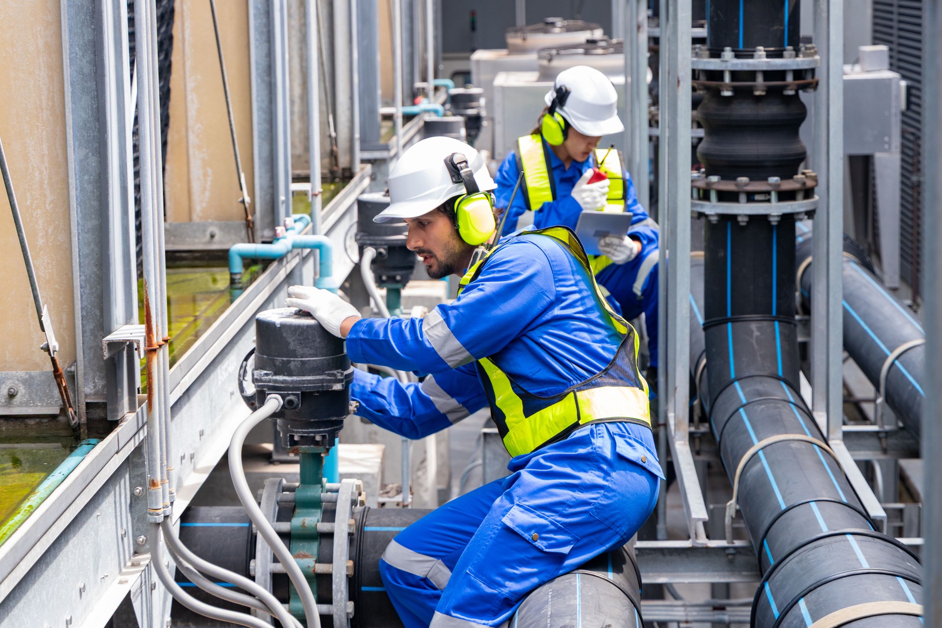 Engineers discussing blueprint near industrial pipes